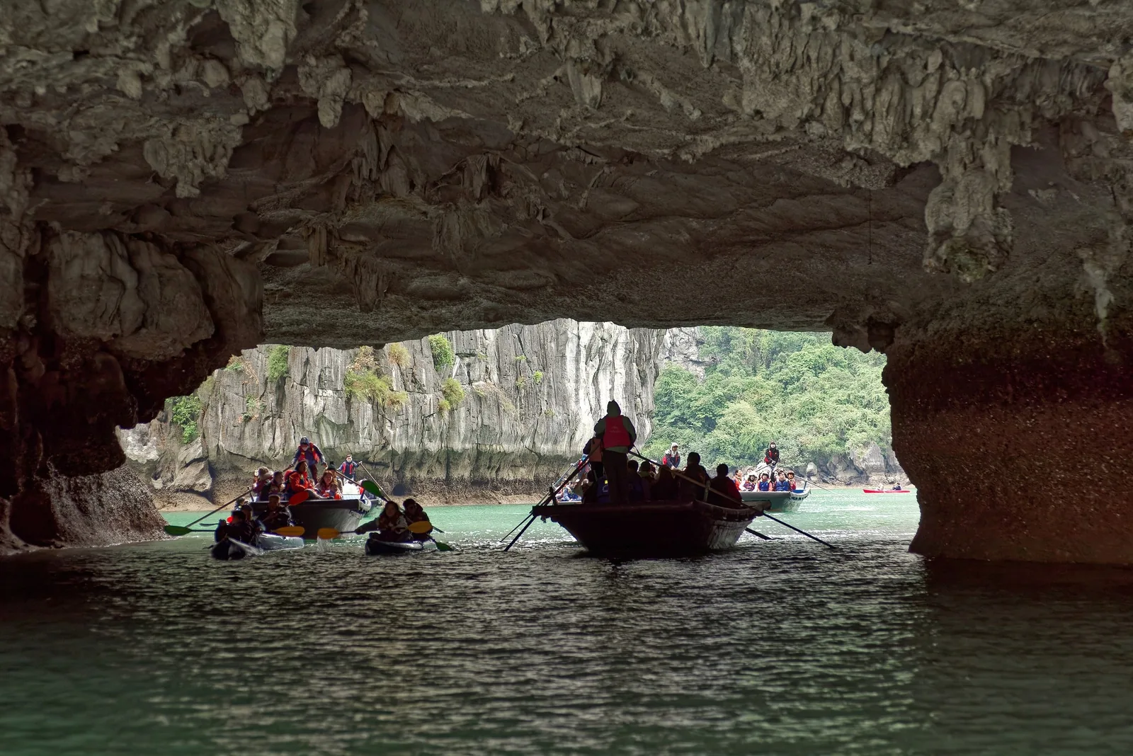 Small boats carrying tourists pass through a rock arch cave into a lagoon in Ha Long Bay.