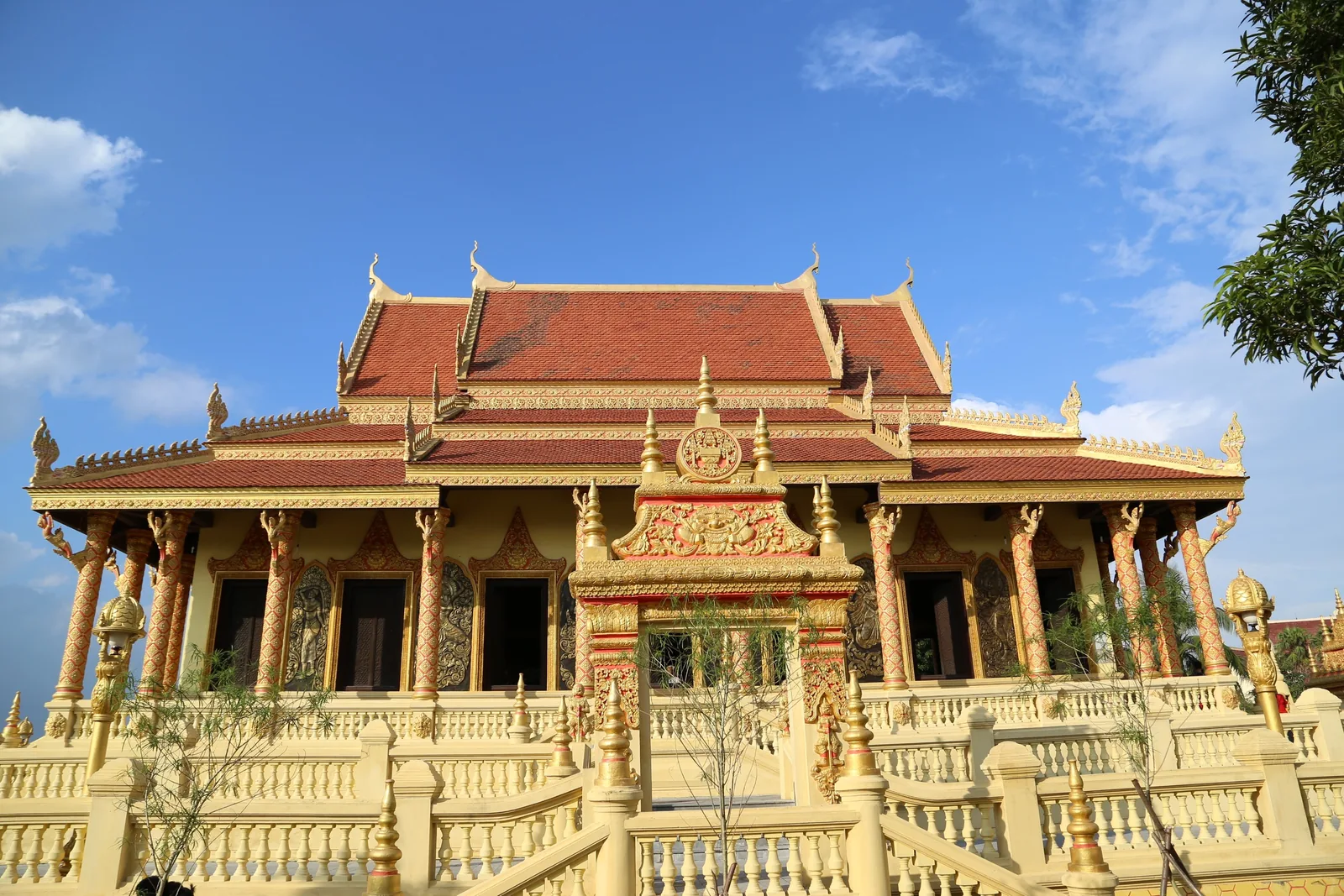 A golden ornate temple with red tiled roof and carved pillars stands beneath a bright blue sky in Vietnam.