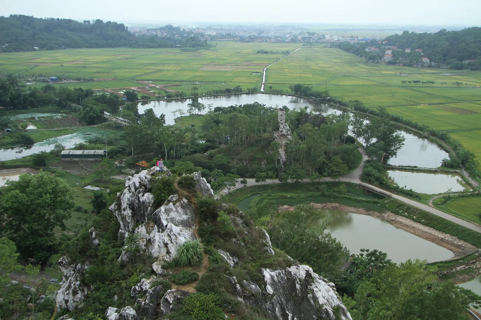 A rocky limestone outcrop overlooks patchwork rice fields and ponds in the countryside near Hanoi.