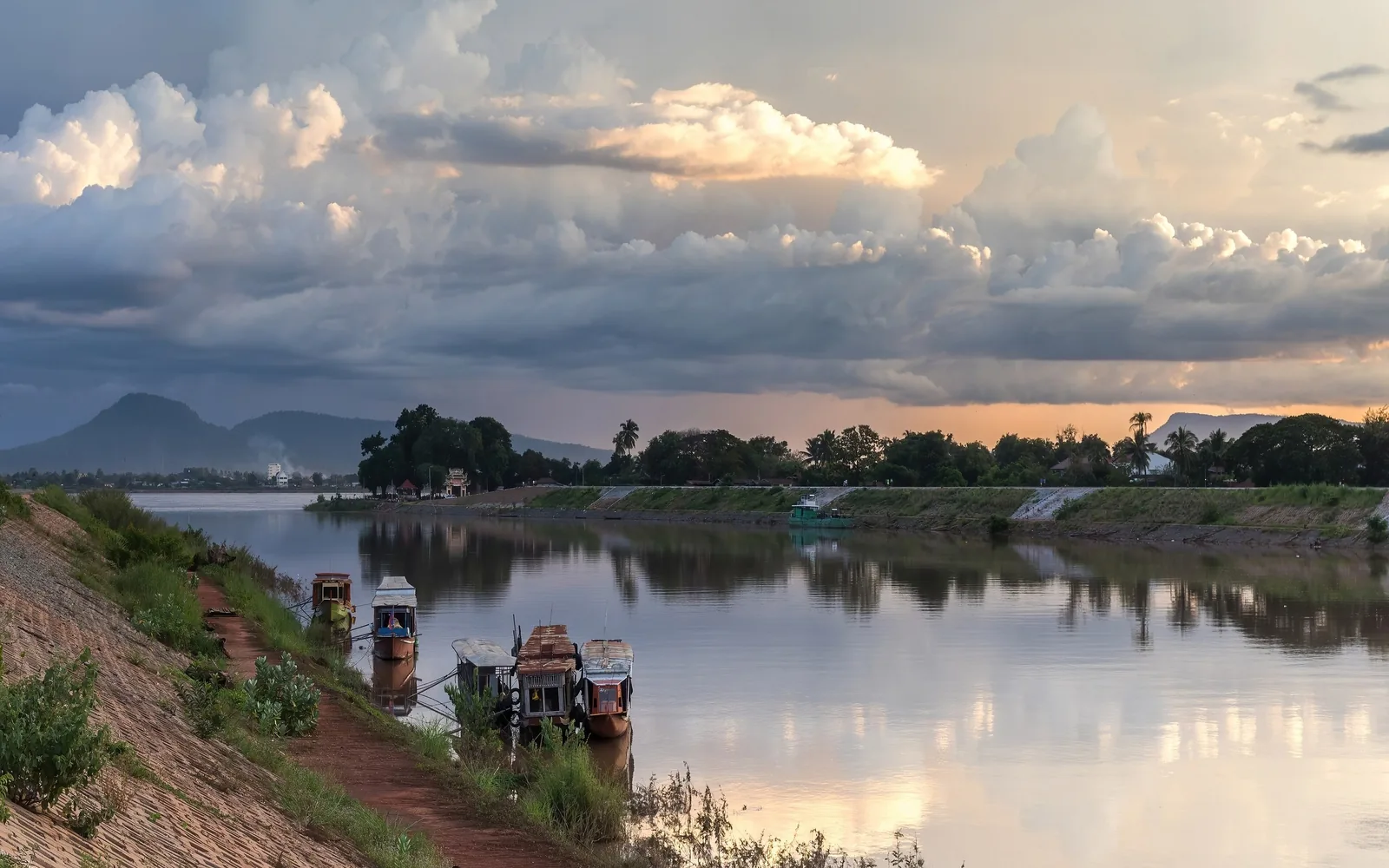 Dramatic clouds at sunset over the Xe Don River with wooden boats moored near Pakse, Laos.