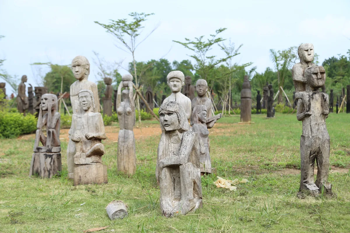 Weathered wooden statues of human figures stand scattered across a grassy field near Hanoi.