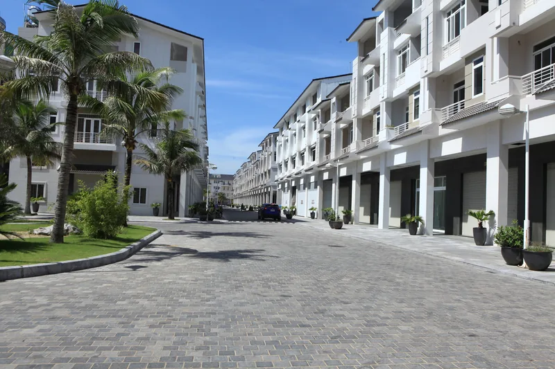 Rows of new white townhouses line a paved street with palm trees on Tuan Chau Island, Ha Long.