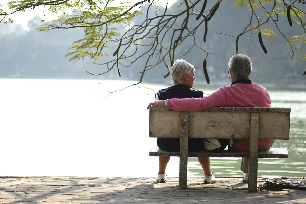 An elderly couple sits together on a bench overlooking a calm lake in Hanoi.