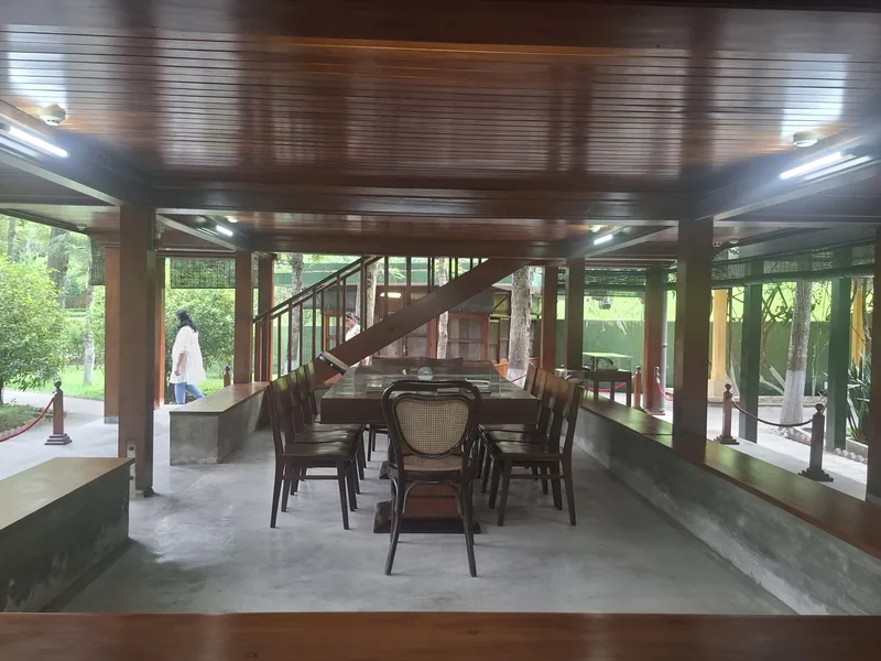 A wooden pavilion with a large table and chairs sits open-air within a garden setting in Hanoi.