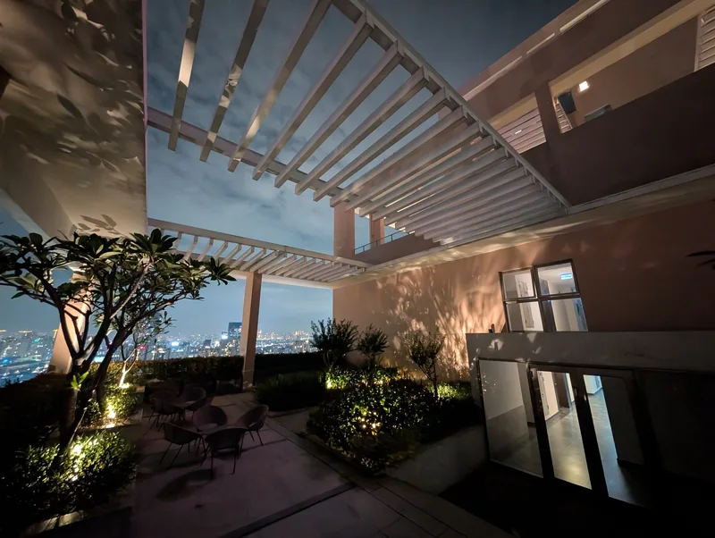 A rooftop terrace with pergola and plants overlooks the illuminated skyline of Ho Chi Minh City at night.