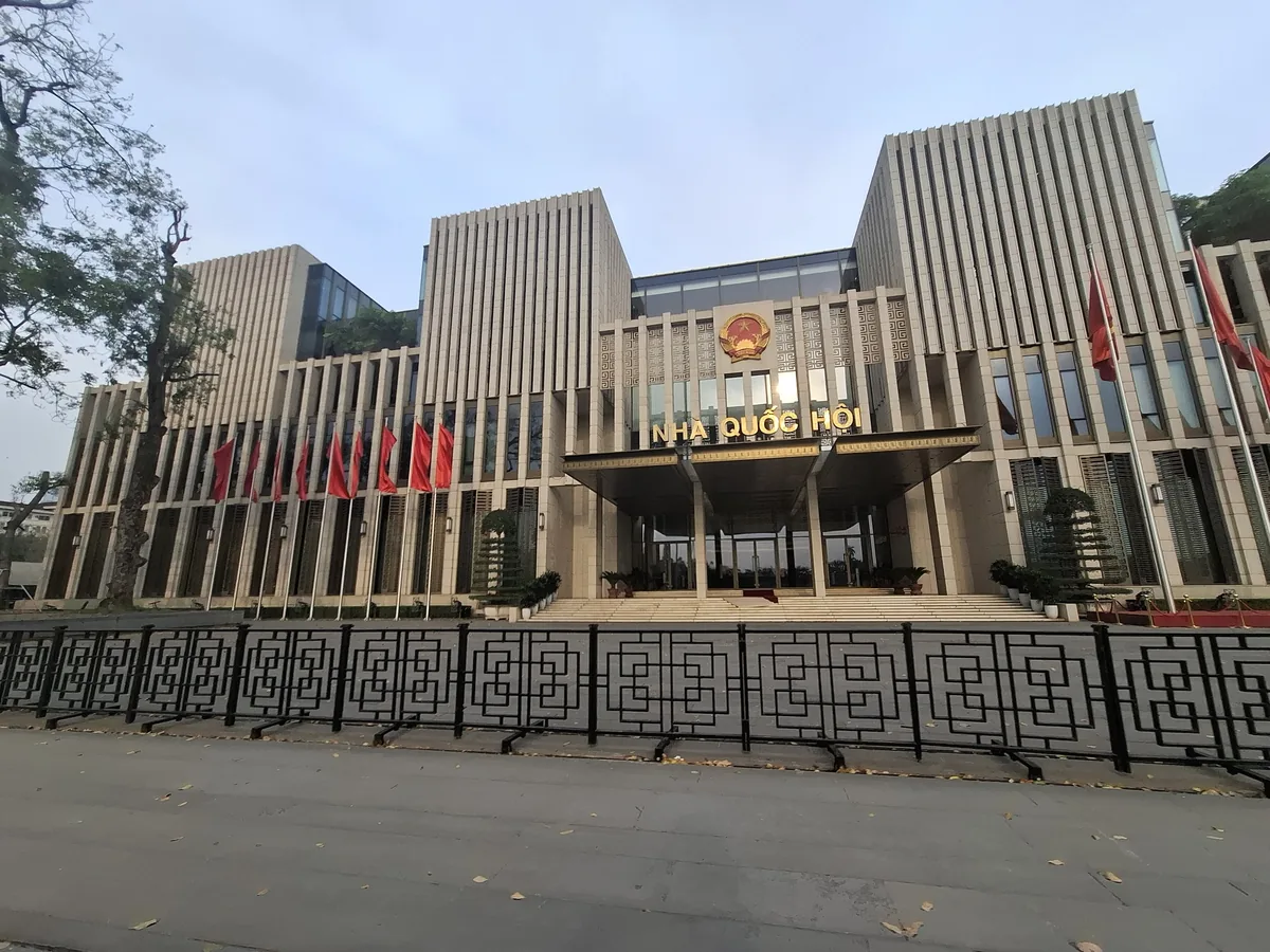 The National Assembly Building in Hanoi with its columned facade and red flags along the front railing.