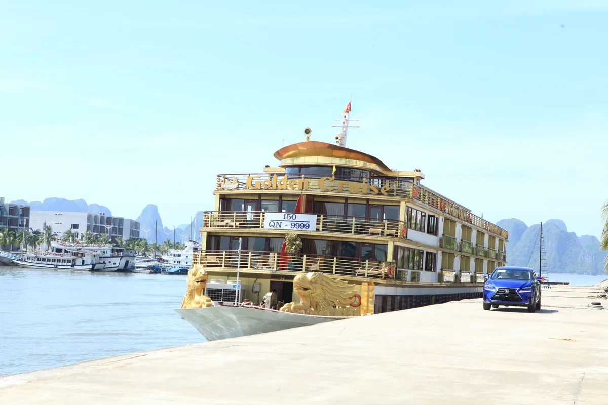 A gold-trimmed multi-deck cruise boat named Golden Cruise docks at Tuan Chau pier in Ha Long Bay with limestone karsts.