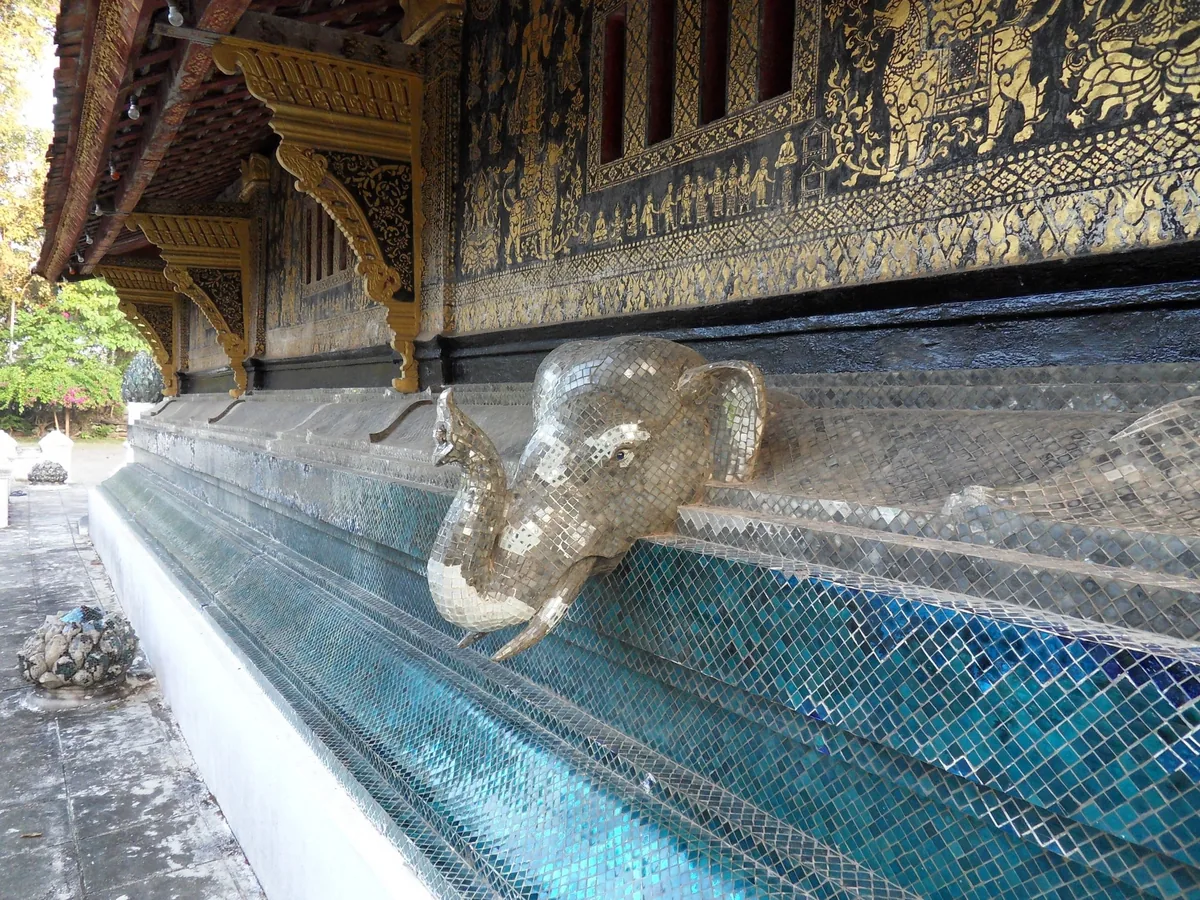 A mosaic elephant head decorates the mirrored temple wall at Wat Xieng Thong in Luang Prabang.