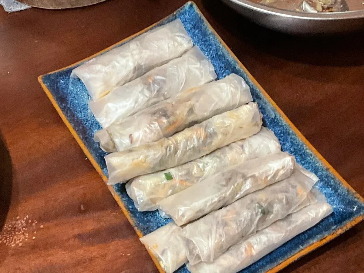 Fresh rice paper rolls filled with vegetables and meat, served on a blue ceramic plate in Hanoi.