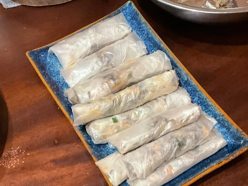 Fresh rice paper rolls filled with vegetables and meat, served on a blue ceramic plate in Hanoi.