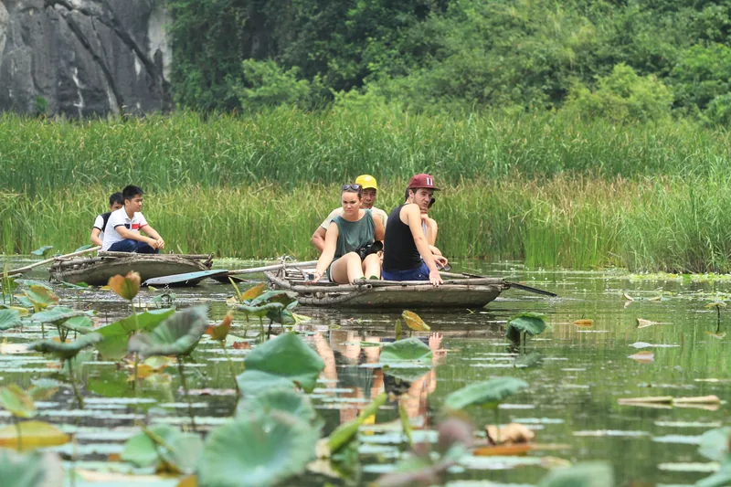 Tourists ride small wooden boats through a lotus pond surrounded by limestone hills near Hanoi.