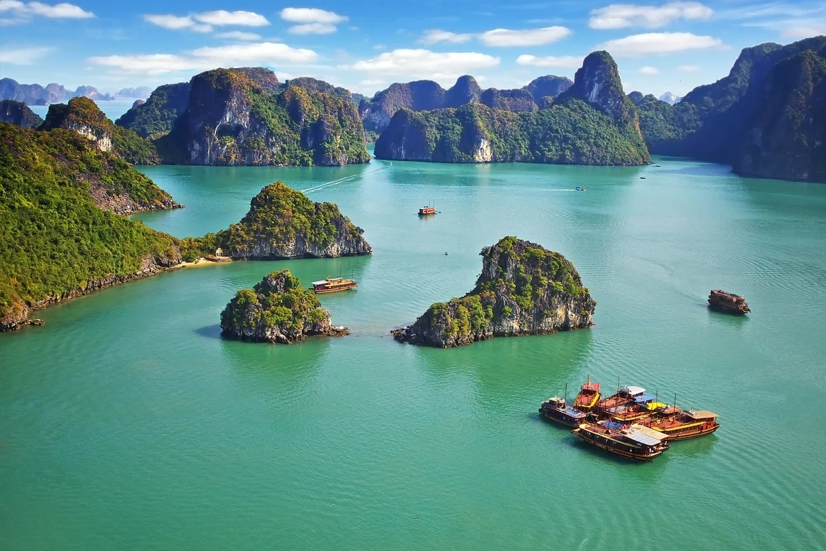 Limestone karst islands rise from turquoise waters with tourist boats scattered across Halong Bay.
