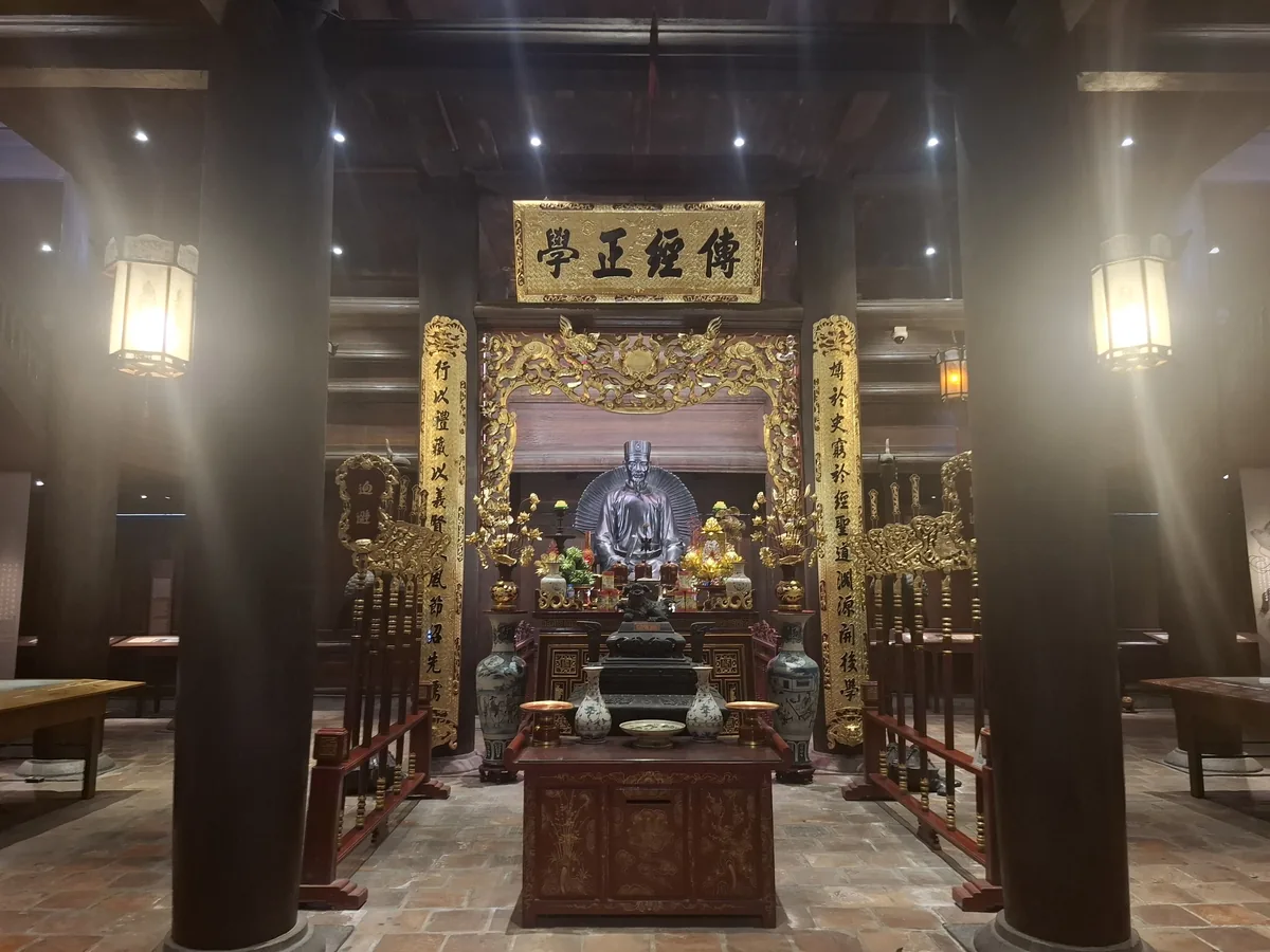 A gilded shrine with a statue and lantern-lit wooden hall inside a temple in Hanoi.