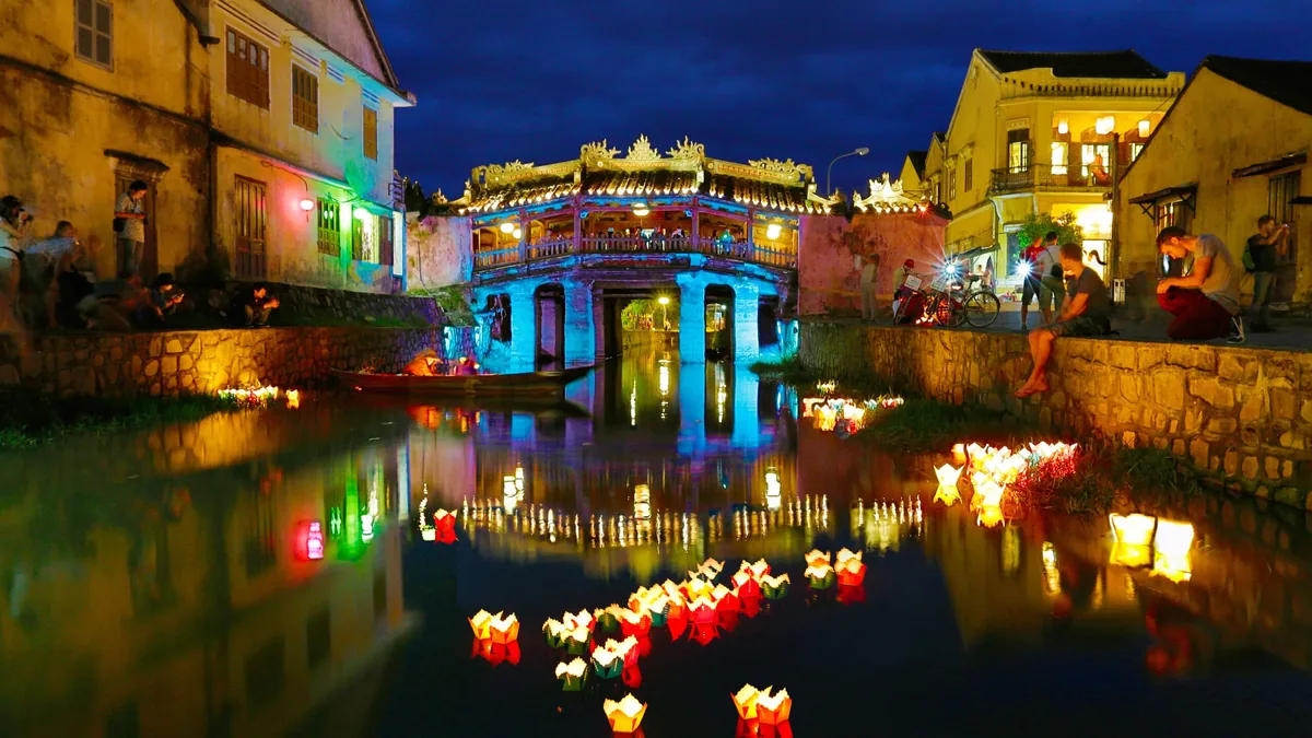 The Japanese Covered Bridge glows blue at night in Hoi An, with floating lanterns drifting on the river below.