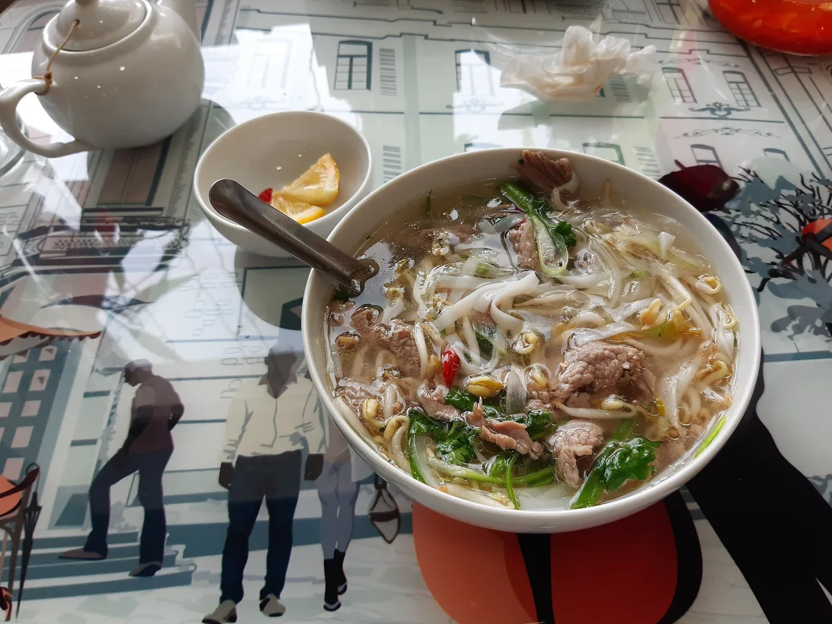 A bowl of Vietnamese pho with beef, herbs and noodles served on a decorated table.