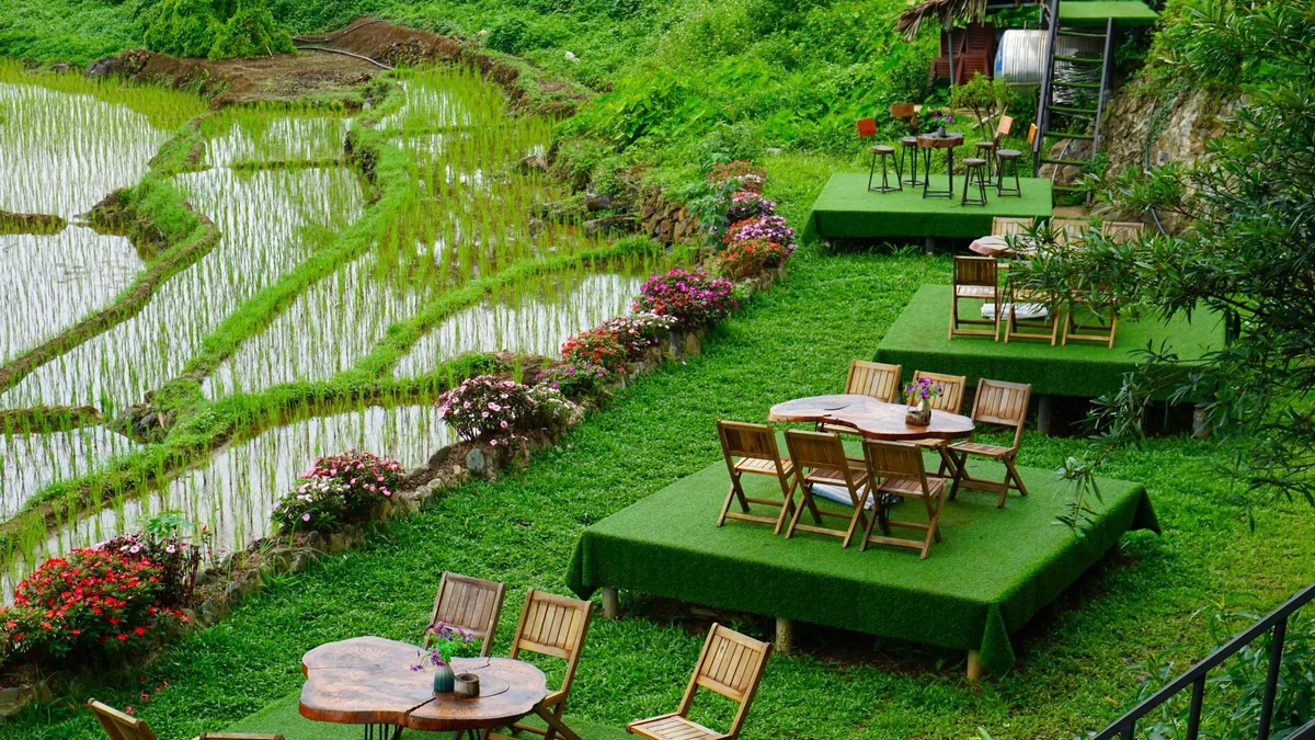 Wooden tables and chairs on grassy terraces overlook flooded rice paddies at a hillside cafe in Pu Luong.