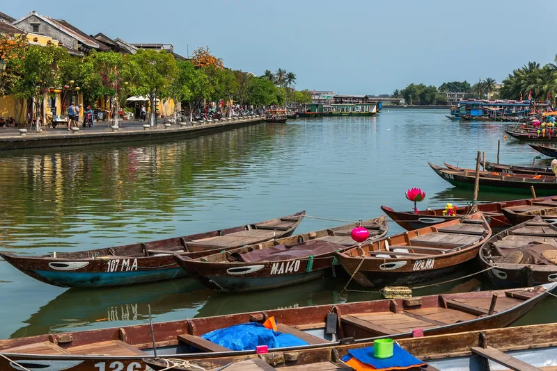 Wooden boats moored along the Thu Bon River beside Hoi An's ancient town waterfront