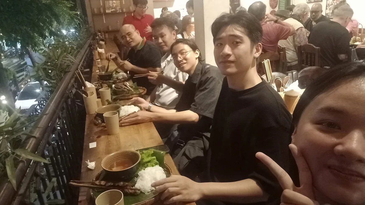 A group of diners sits at a wooden counter enjoying a meal at a busy restaurant in Hanoi.