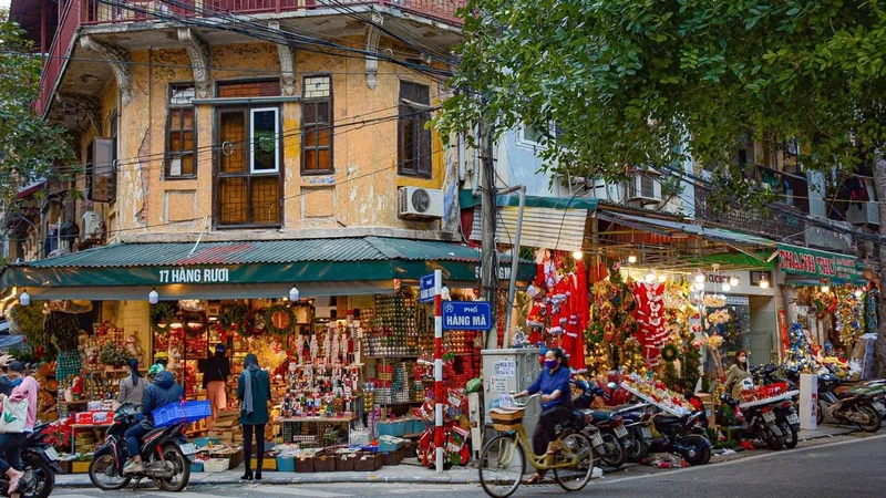 A weathered corner building on Hàng Mã street in Hanoi's Old Quarter displays colorful festive decorations and busy street.
