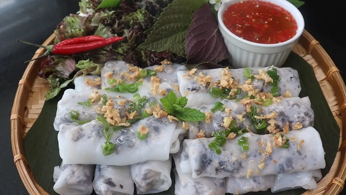 Steamed rice rolls topped with fried shallots and herbs served on a woven tray with chili dipping sauce in Hanoi.