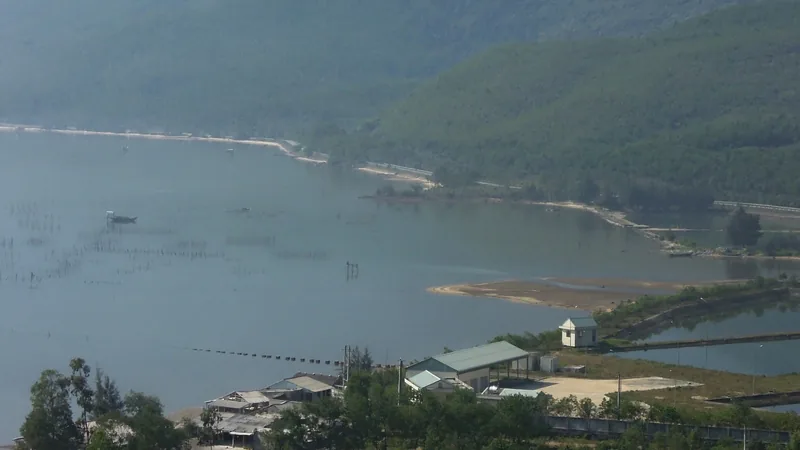 A misty lagoon with oyster farming stakes and coastal buildings, seen from a hillside in Thua Thien Hue province.