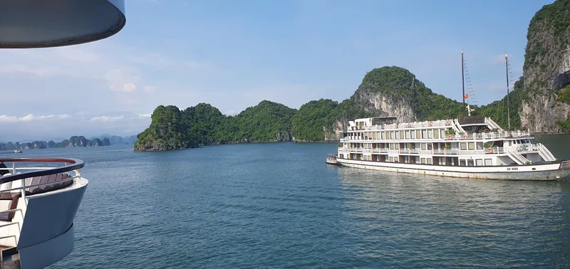 A multi-deck cruise ship anchors near limestone karsts under a clear sky in Halong Bay.