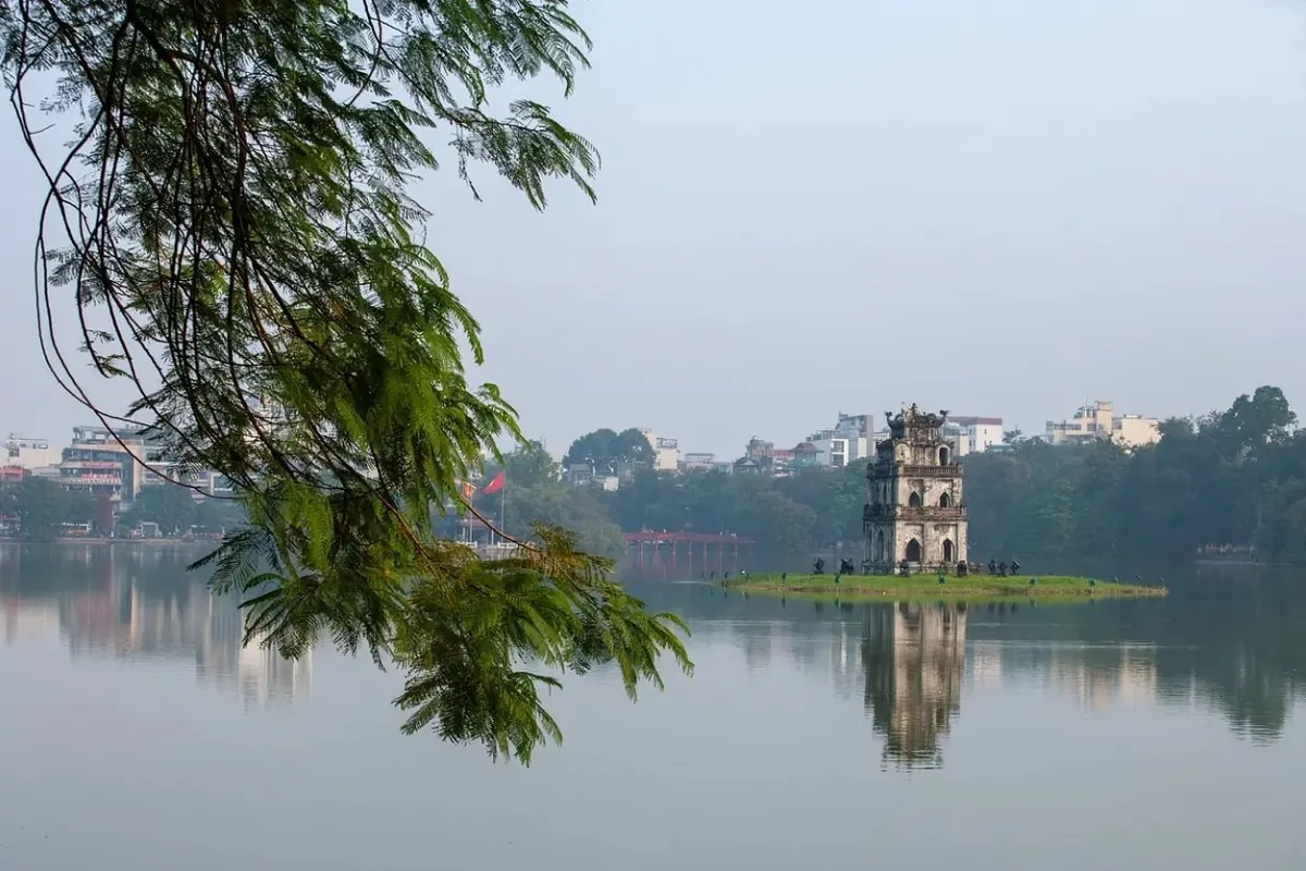 Turtle Tower stands on a small islet in Hoan Kiem Lake, framed by hanging tree branches in Hanoi.