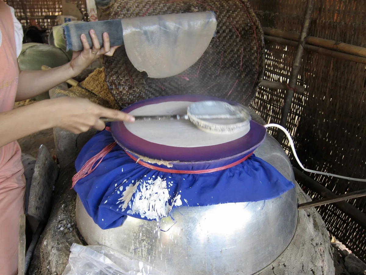 A woman spreads rice batter over a cloth-covered steamer to make traditional Vietnamese rice paper.