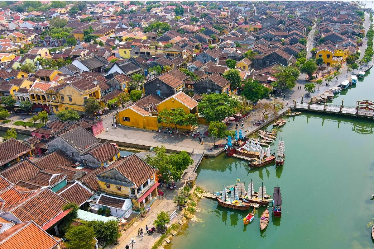 Aerial view of Hoi An Ancient Town's red-tiled roofs and yellow houses along the riverbank with wooden boats moored on the.