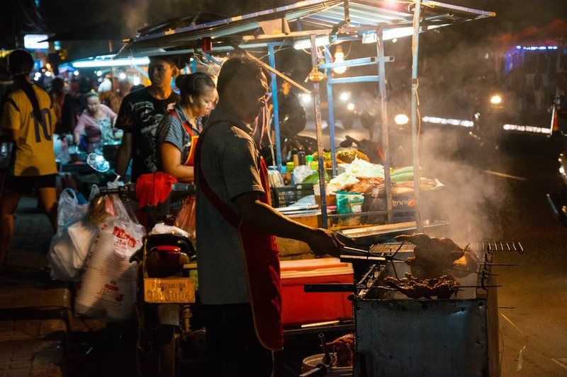 Street vendor grilling skewers over charcoal at a night market