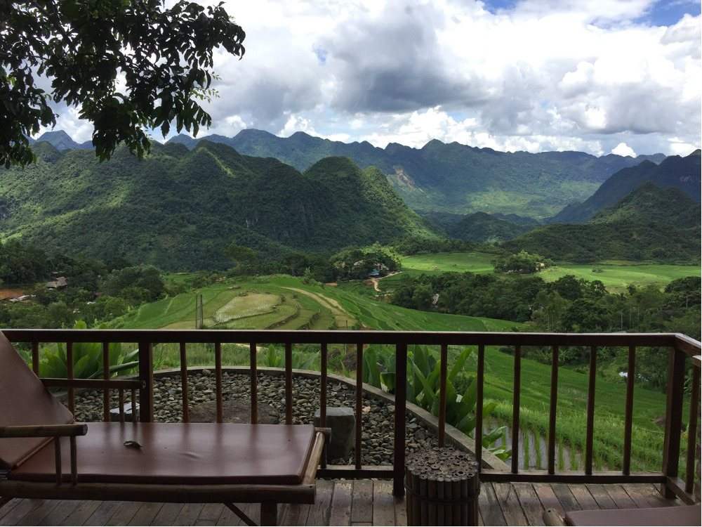 View from a wooden lodge balcony over rice fields and mountains
