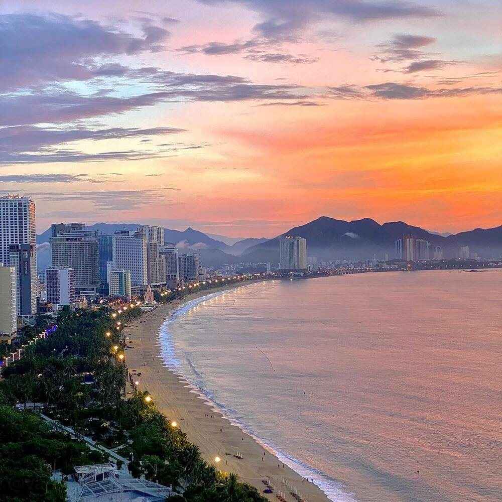 Nha Trang bay curving past high-rise hotels under a pink sunset sky