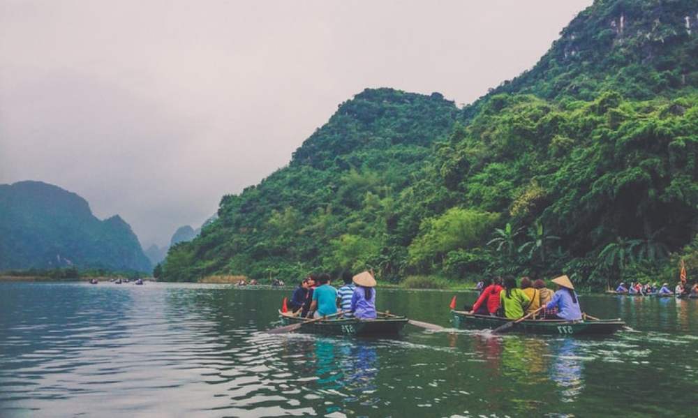 Small tour boats moving up a green river between forested karst