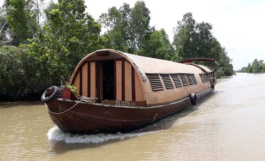 Covered wooden cruise boat on a narrow palm-lined channel