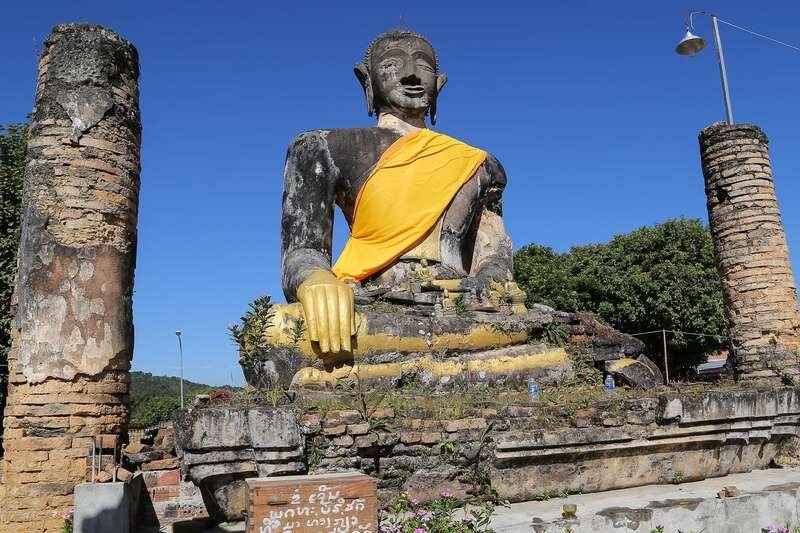 Seated Buddha draped in saffron cloth among ruined brick columns